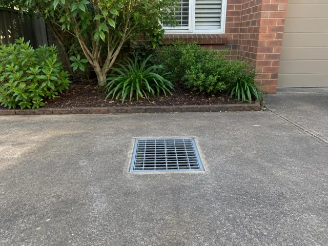 Flush stormwater grate in a concrete driveway beside brick wall and garden in Pennant Hills